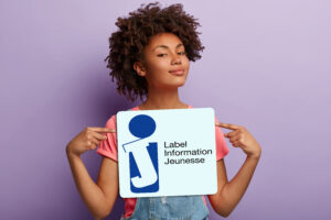 Une jeune femme tient dans entre les mains le panonceau montrant le label Information Jeunesse délivré par l'Etat